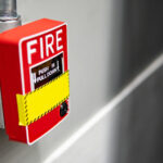 Red fire alarm switch on concrete wall in factory. Industrial fire warning system equipment for emergency.